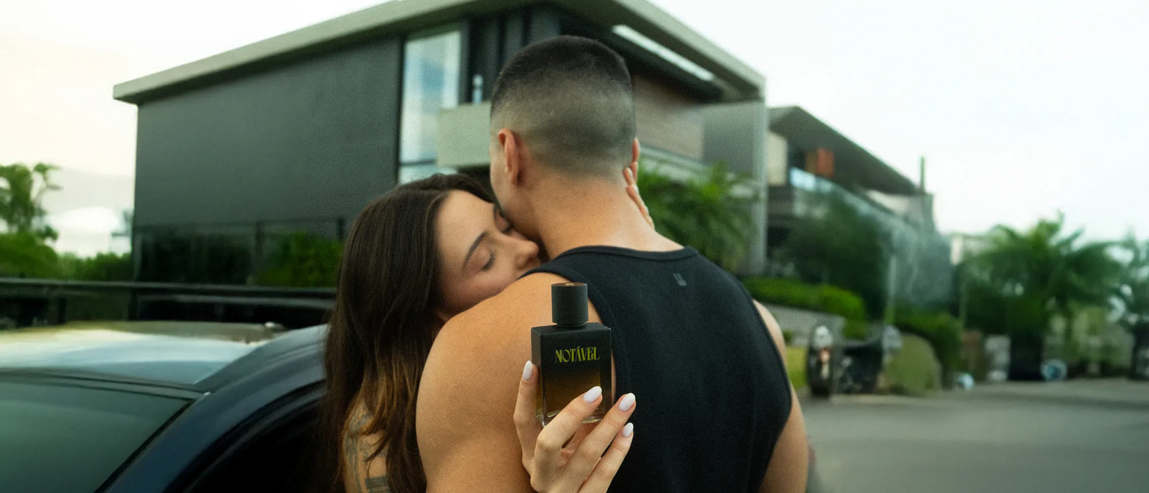 Mulher abraçando um homem que segura um frasco do Notável
